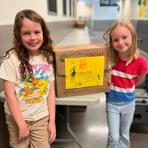 Two students stand with a box of goods donated during the Harvest of Love donation drive.